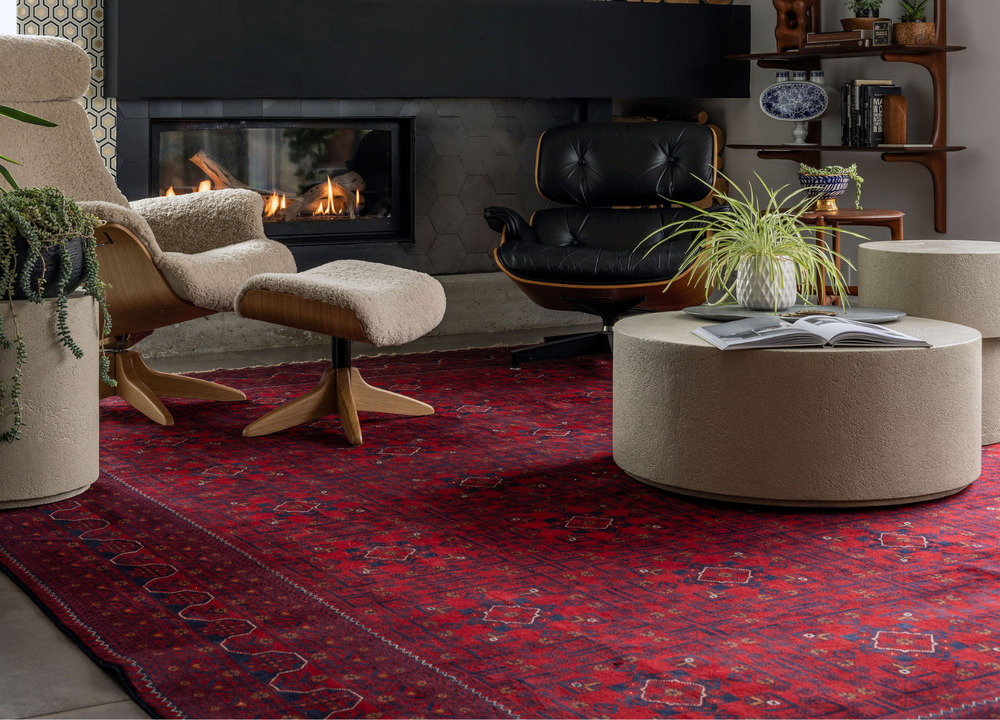 Afghan hand made rug with rich red geometric patterns, styled in a cozy living room with modern furniture, including a Tuck Rugs leather chair, ottoman, and fireplace.