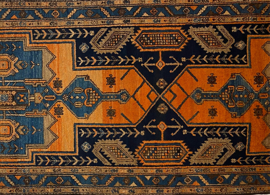 Close-up view of The Loch Rug's intricate hand-knotted geometric designs, showcasing vibrant orange and blue hues. Available at Tuck Rugs.