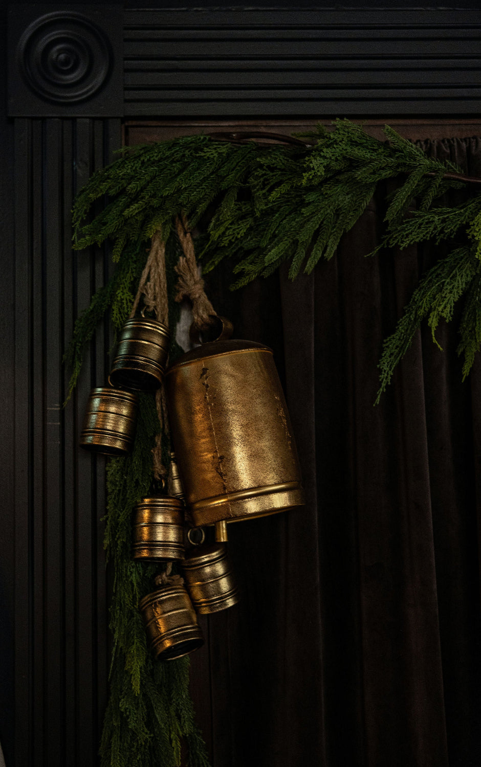 Decorative brass bells hanging from a green branch against a dark background