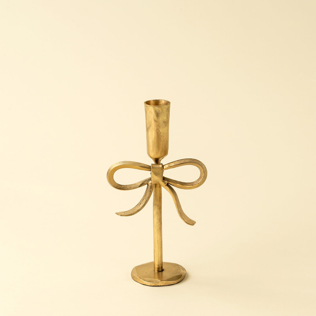 Gold candle holder with bow design on a beige background