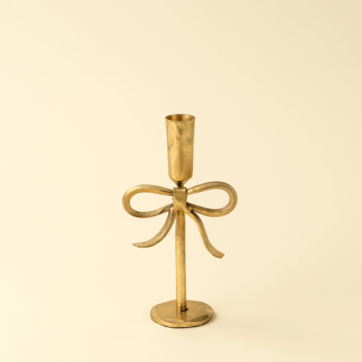 Gold candle holder with bow design on a beige background