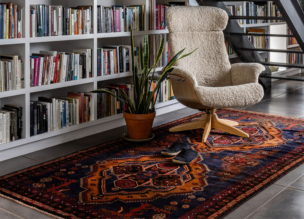 The Peninsula Afghan wool rug styled in a cozy reading nook, featuring vibrant geometric patterns in navy and orange tones. Available at Tuck Rugs.