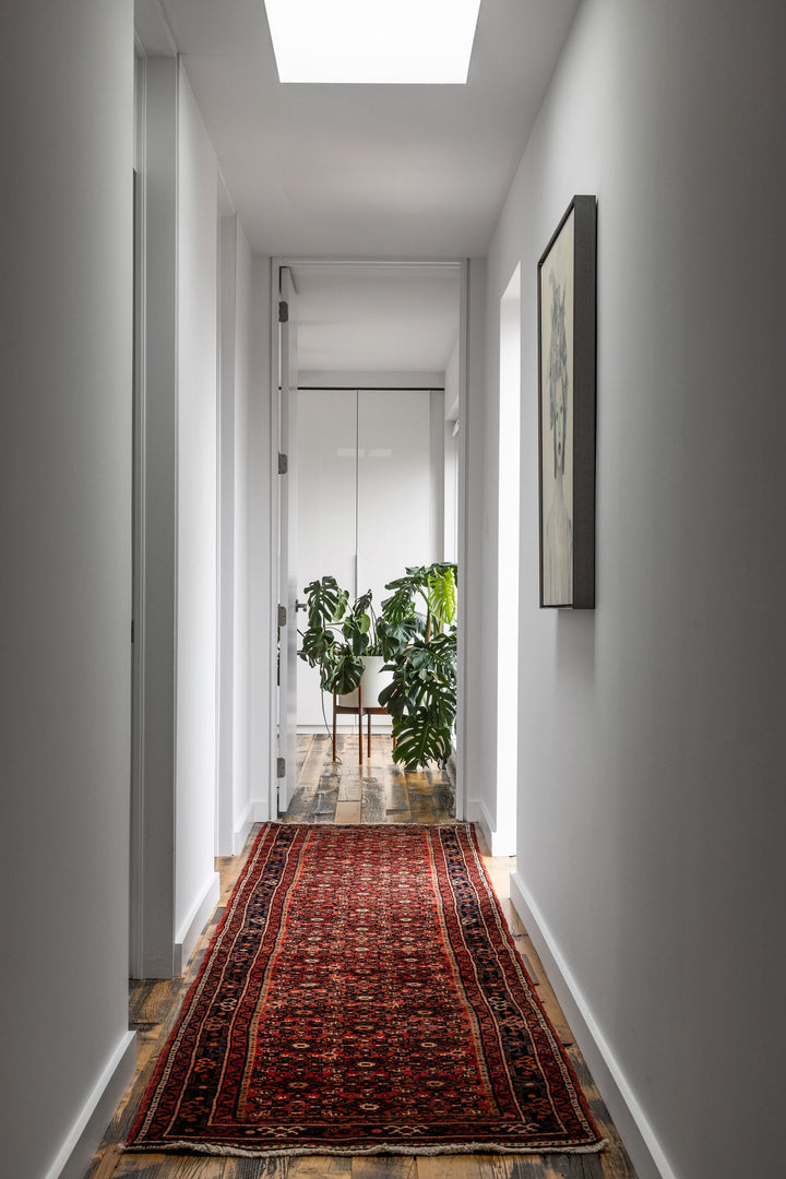 The Crown Rug shown in a long hallway, featuring detailed geometric patterns and a rich red palette. Available at Tuck Rugs.